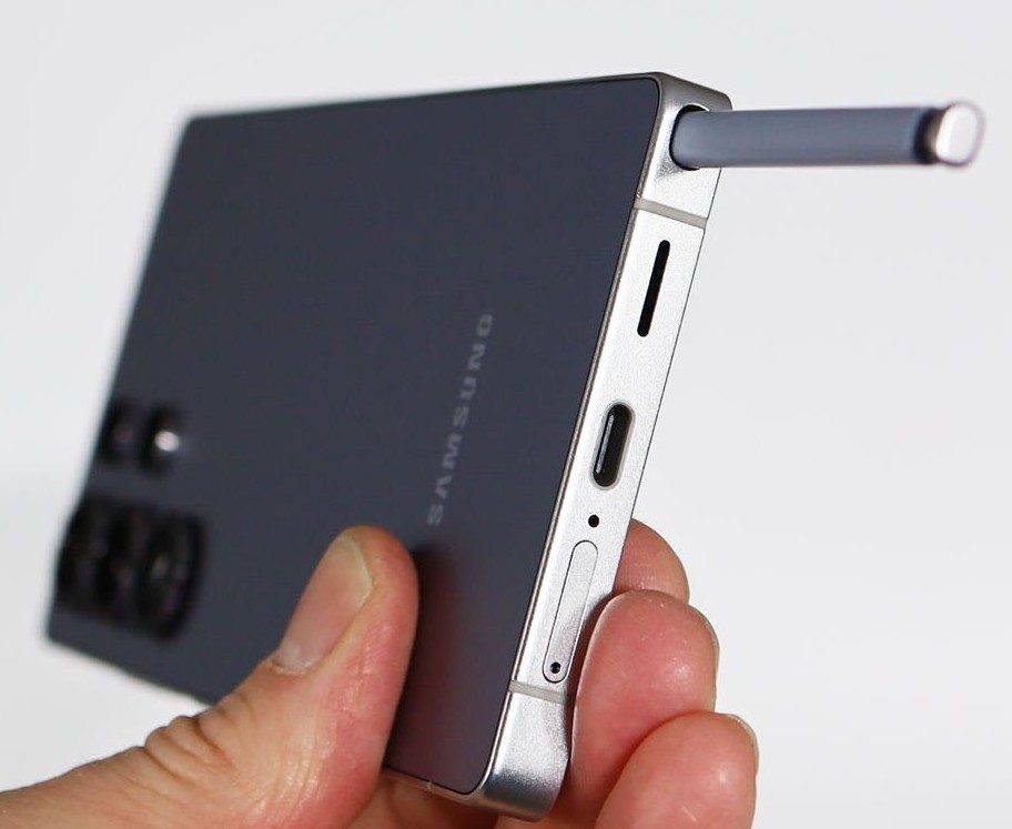 Стилус S Pen наполовину выдвинут из гнезда в корпусе Samsung Galaxy S26 Ultra, смартфон держат в руке